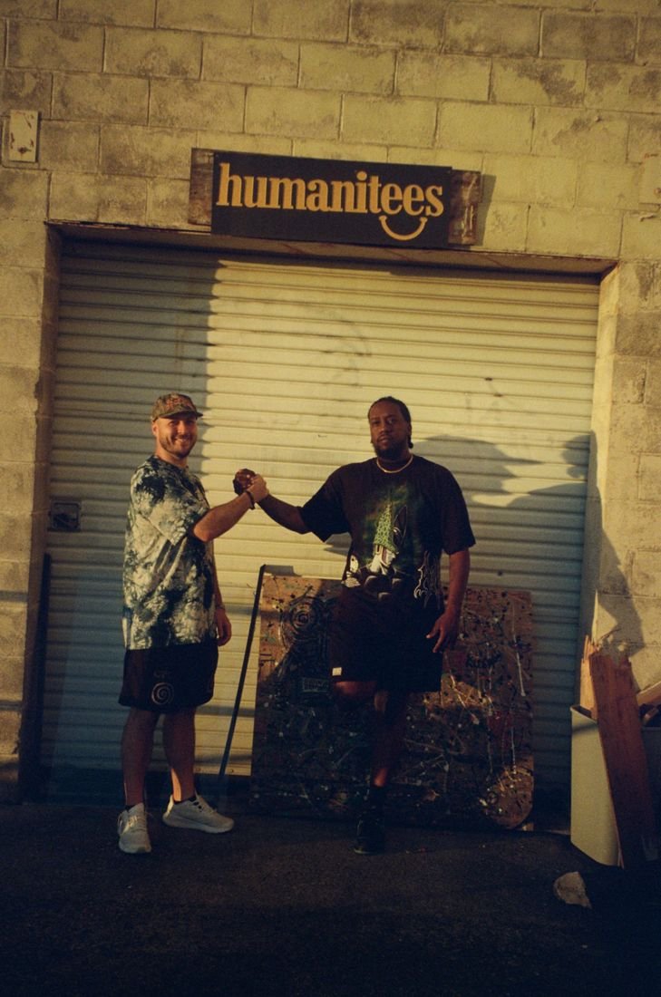 Two of the Humanitees crew outside the shop, under the Humanitees sign